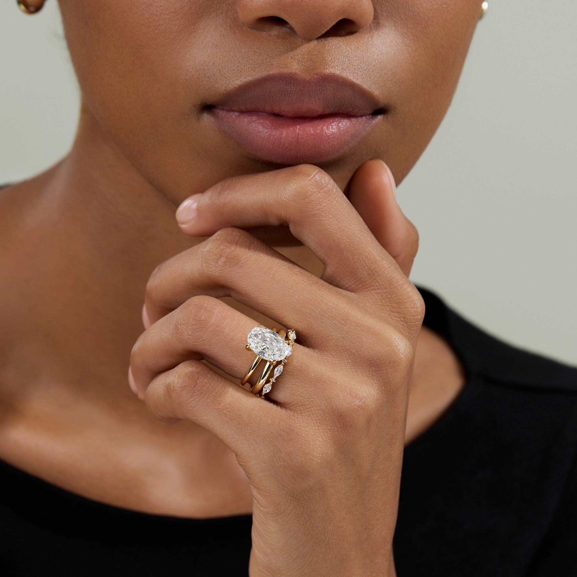 A close-up of a model wearing a gold ring with a large oval-cut clear gemstone and smaller accent stones, Solitaire engagement ring, Oval cut Engagement Ring, Elongated, eamti, travel ring, eamti jewelry